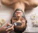 Spa accessories wellness setting with cosmetic bottles and salt with white plumeria flower, blurred massage stones in wooden bowl in background, spa concept, copy space